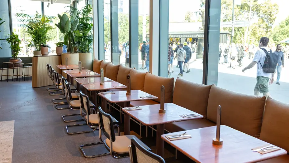 Window-side tables with banquette seating, overlooking MCG concourse crowds