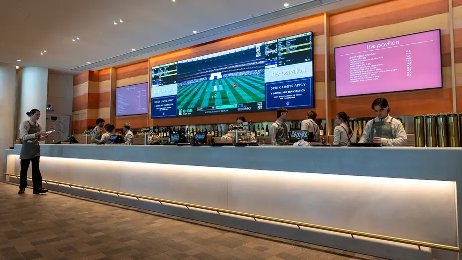 Staff serving behind the bar, with cricket on screens above