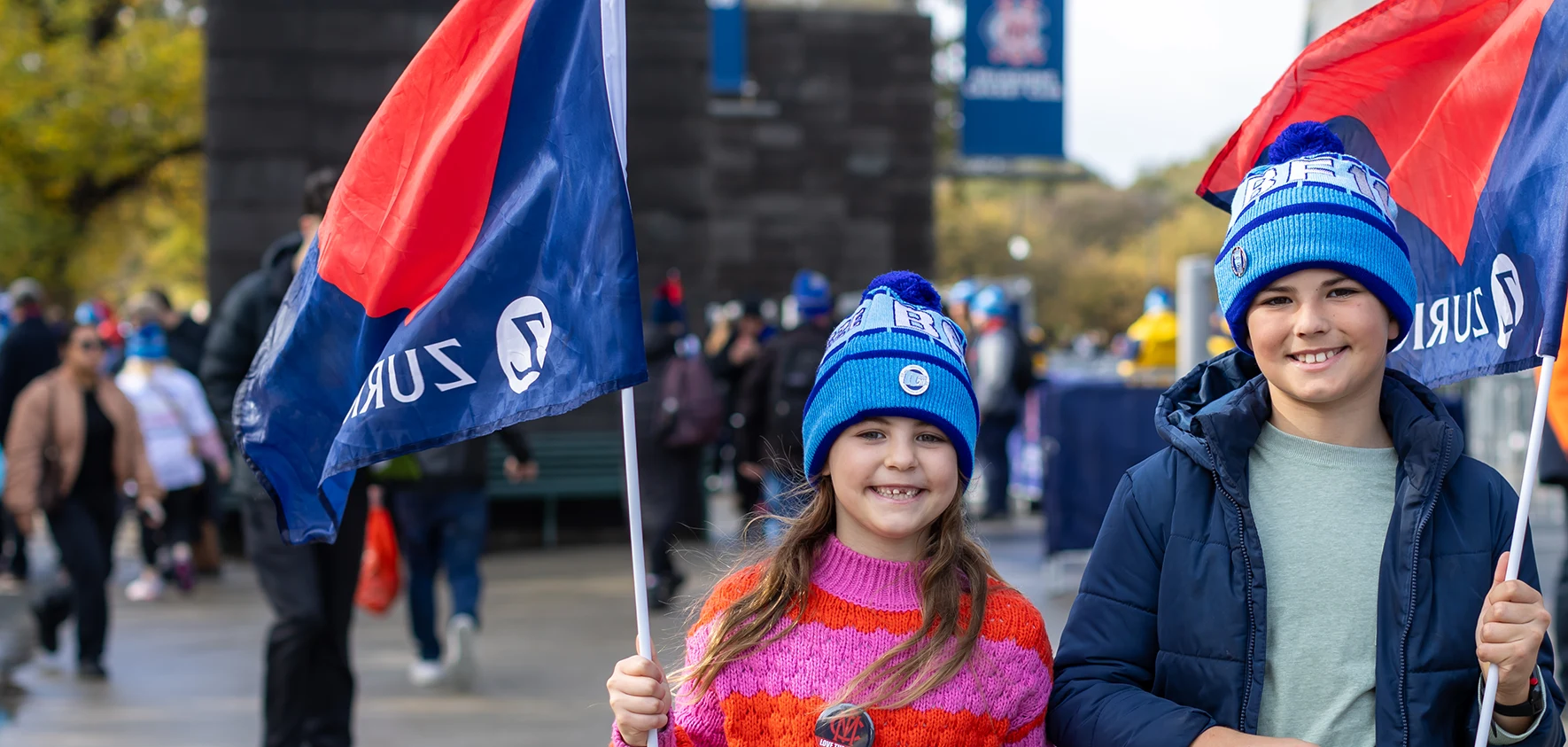 Two young fans wave Melbourne Football Club flags outside the MCC Gate 2