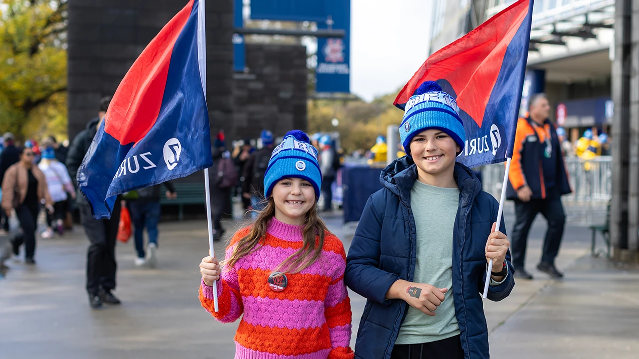 Two young fans wave Melbourne Football Club flags outside the MCC Gate 2