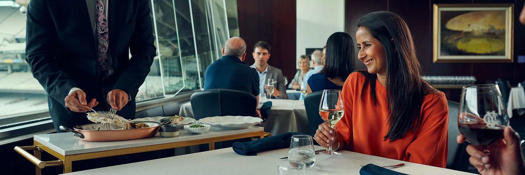 Waiter serving a smiling guest at a fine dining restaurant overlooking a stadium