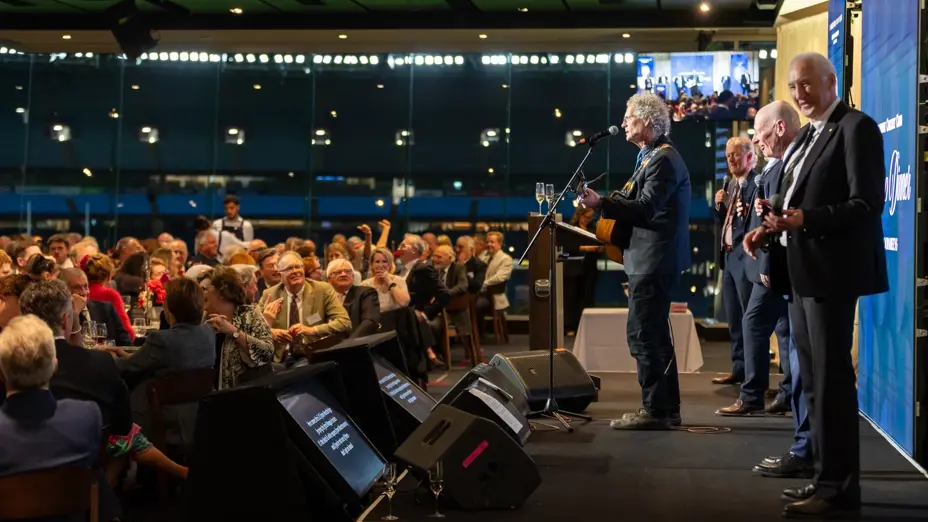Large seated audience watching the Coodabeens sing and play guitar
