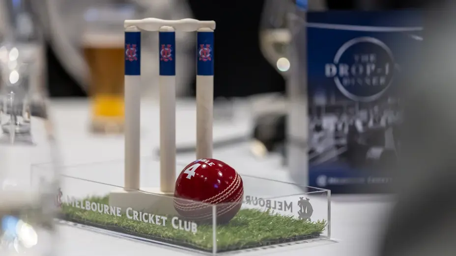 Table centrepiece of MCC-branded cricket stumps and ball, with a Drop-In Dinner sign behind.