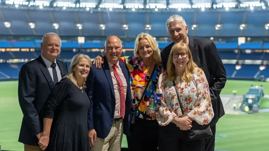 Six guests pose for a photo with the floodlit MCG arena behind them