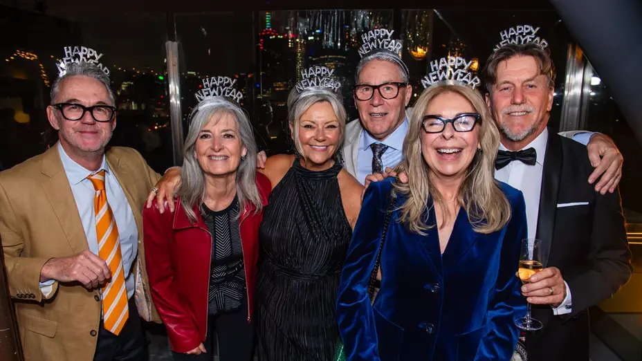 Six guests wearing "Happy New Year" tiaras smiling together