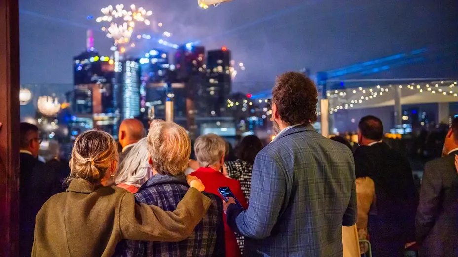 Guests watching New Year's Eve fireworks over the Melbourne city skyline from an MCG balcony